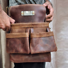 Brown leather tool bag held by a person with a neutral background