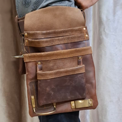 Brown leather bag with gold hardware held by a person against a neutral background
