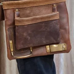 Brown leather bag with gold hardware held by a person against a neutral background