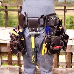 A person wearing a brown leather work belt with multiple pockets, equipped with tool holders for a hammer and other construction tools.