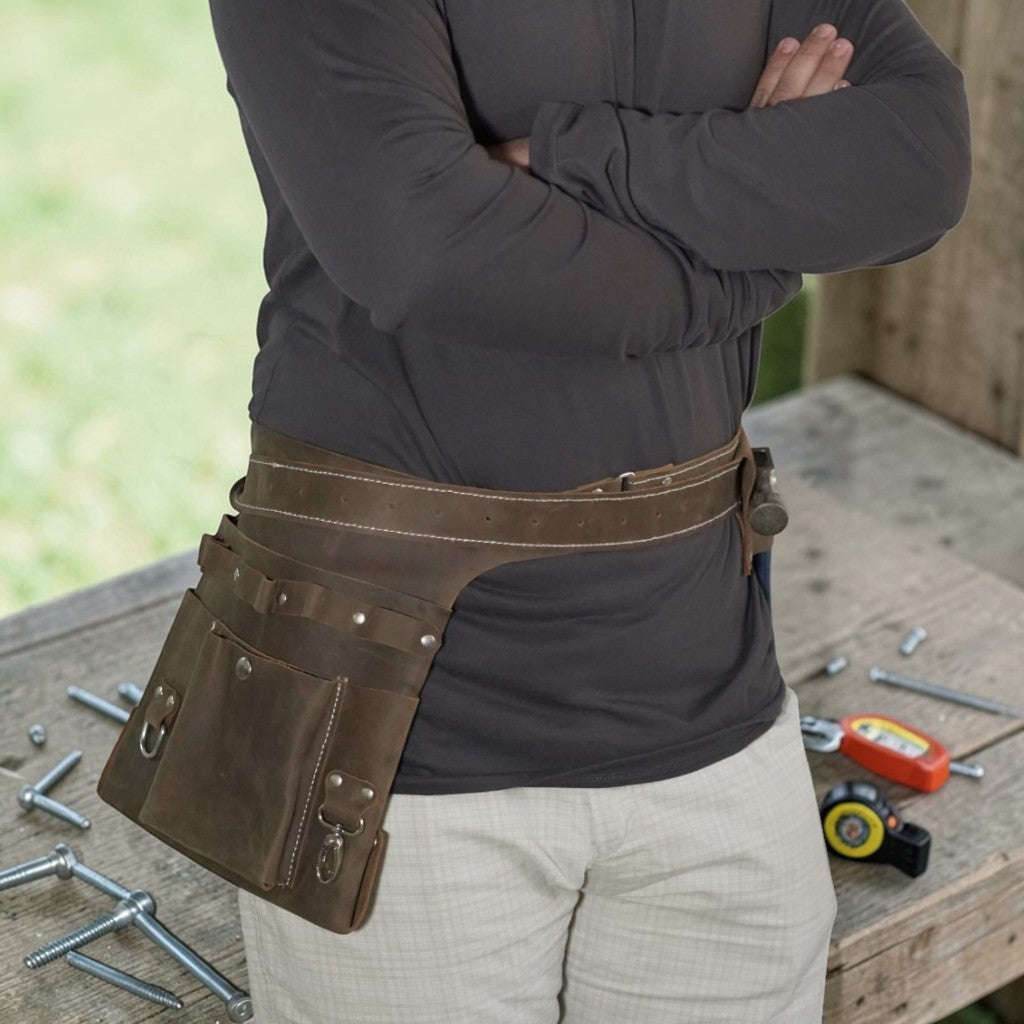 Person wearing a brown leather tool belt with tools on a wooden surface.