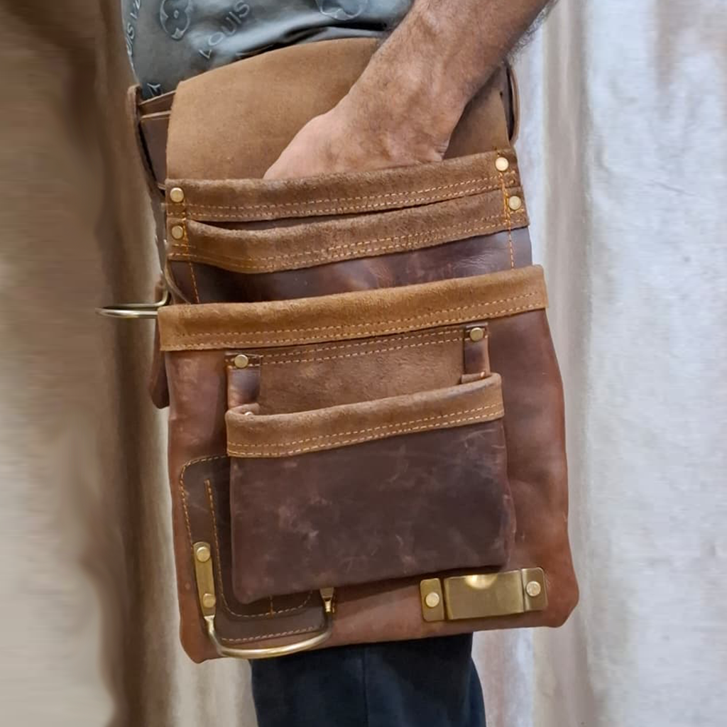 Brown leather bag with gold accents held by a person against a neutral background